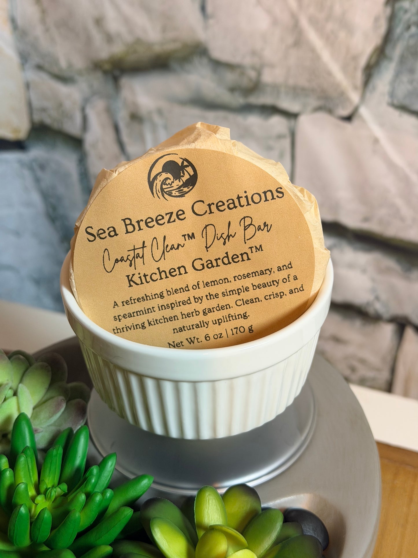 Jar with a wooden lid featuring Sea Breeze Creations branding, set against a stone wall and green plants.