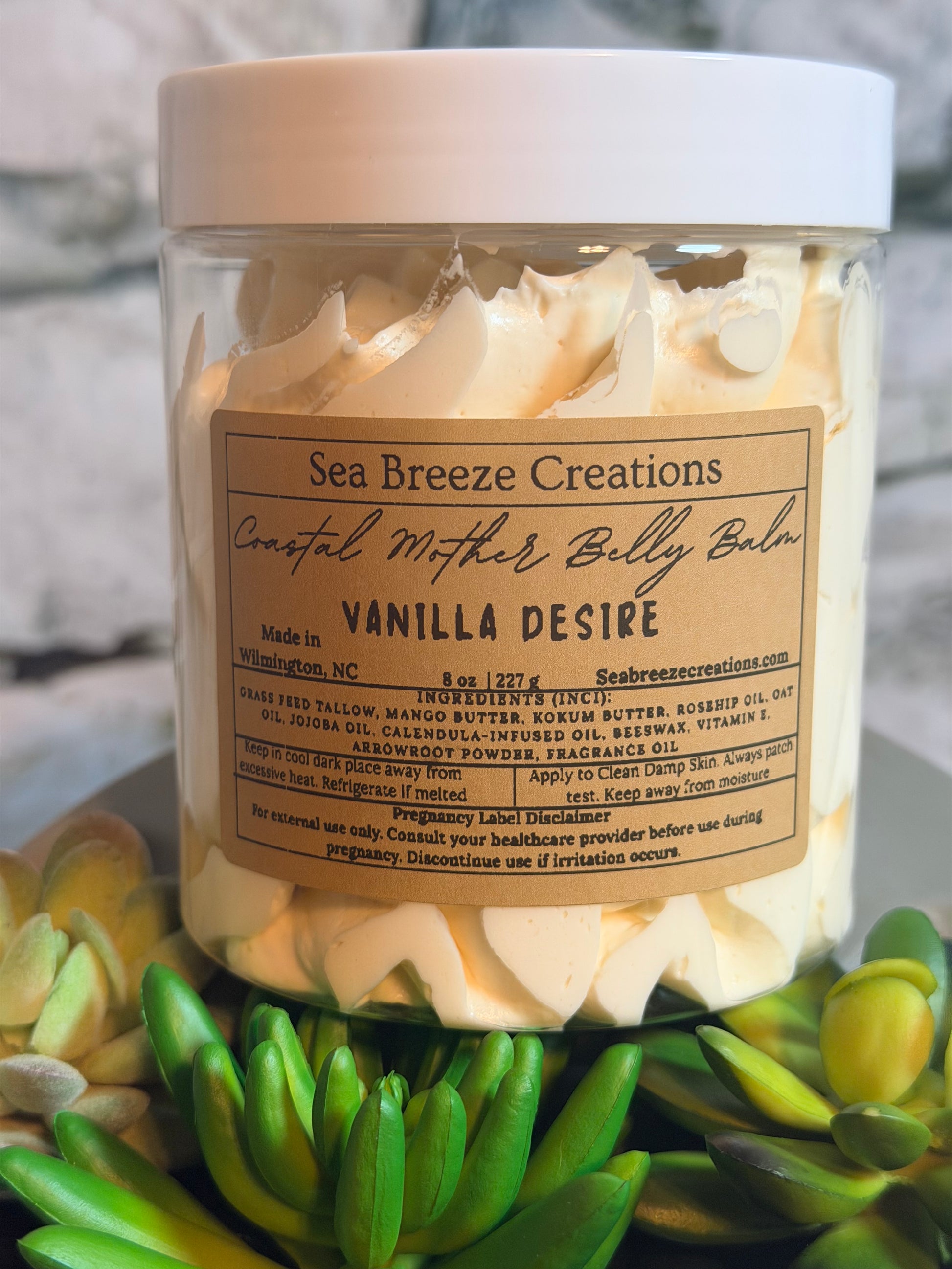 Jar of vanilla- coastal mother belly balm with a label, surrounded by greenery.