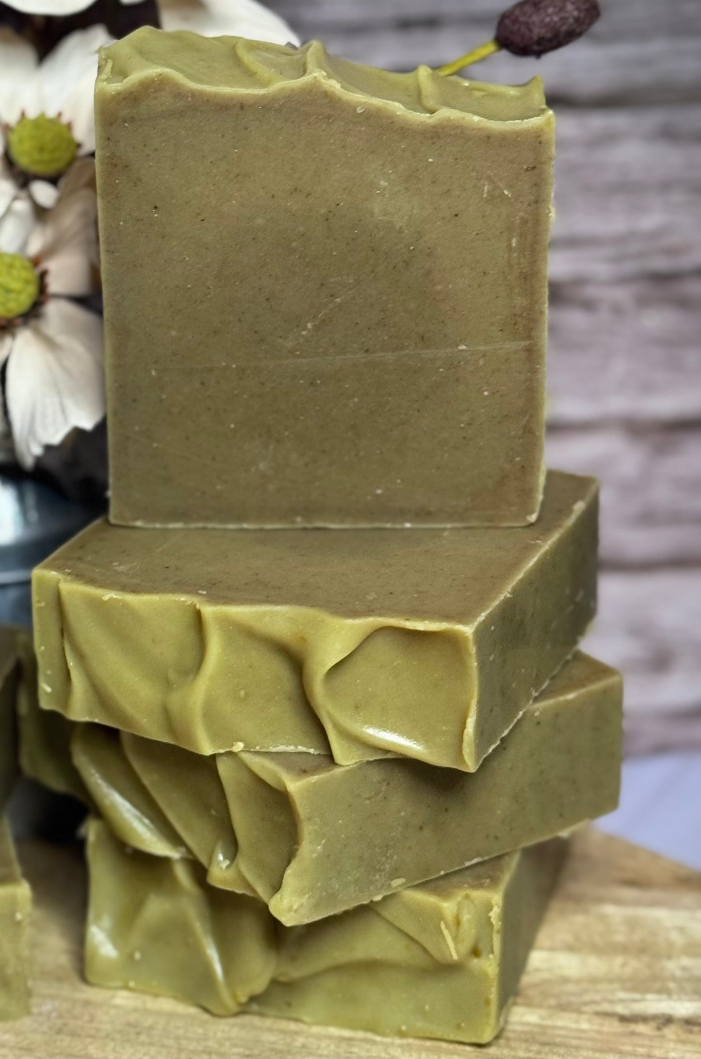 Stack of green soap bars on a wooden surface with a blurred natural background