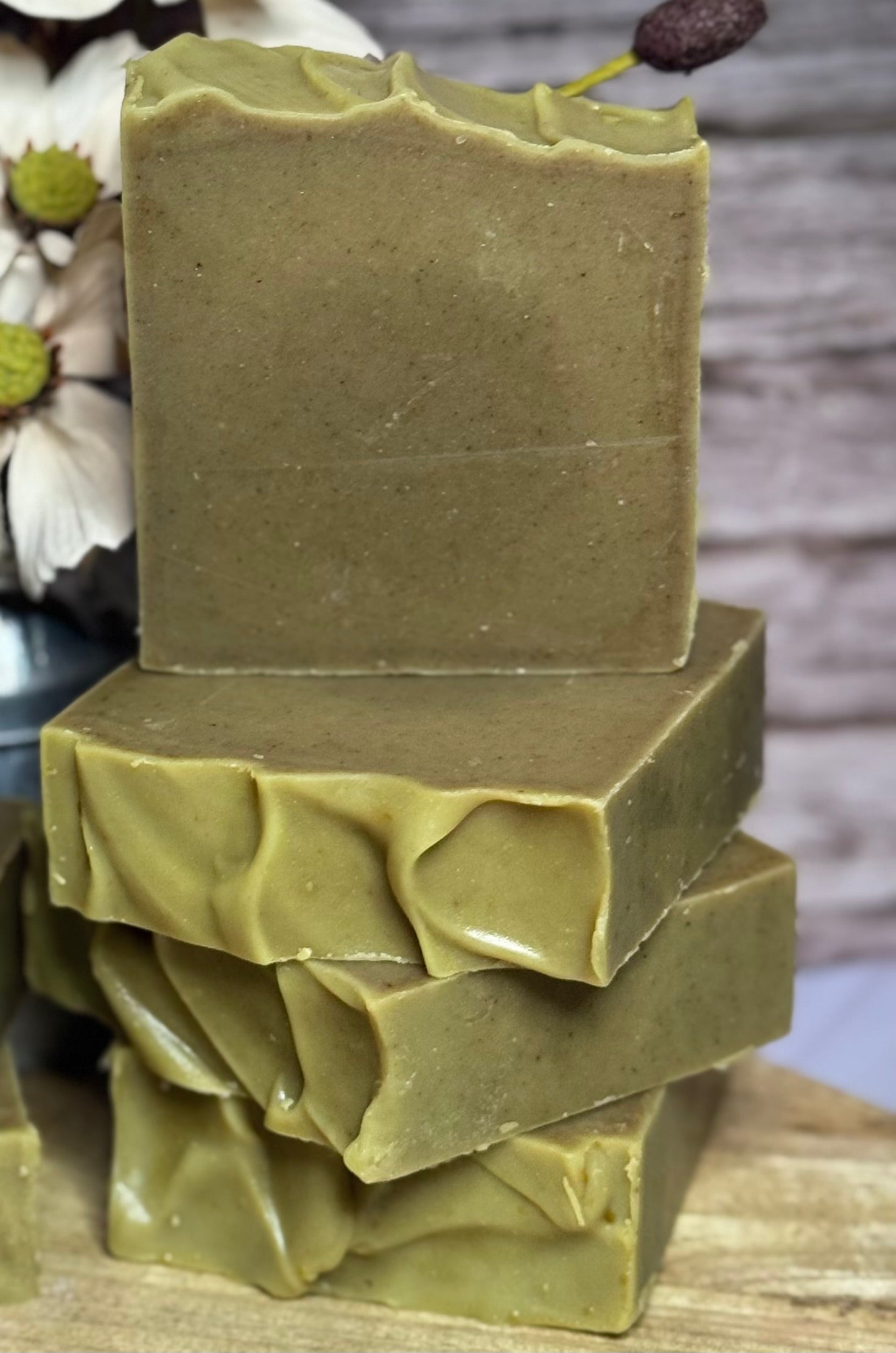 Stack of green soap bars on a wooden surface with a blurred natural background