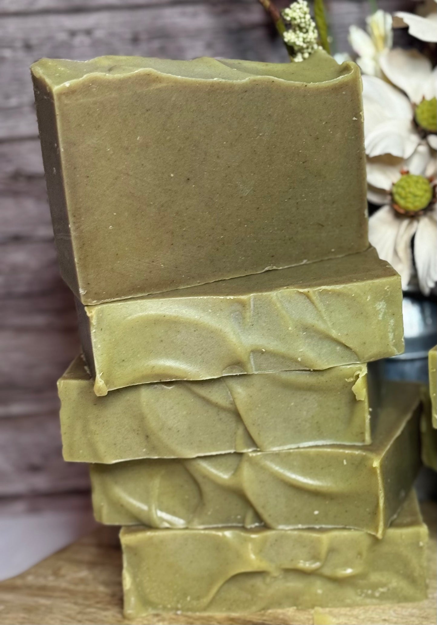 Stack of green soap bars on a wooden surface with a blurred natural background