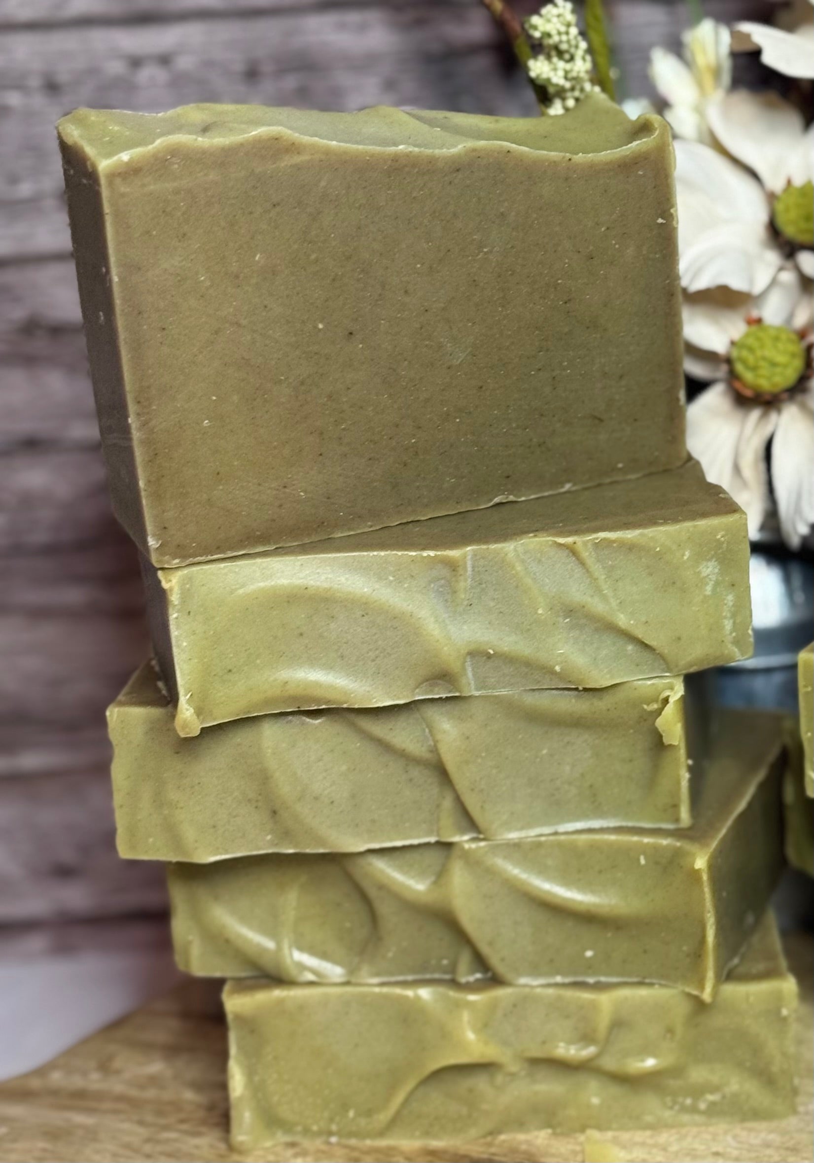 Stack of green soap bars on a wooden surface with a blurred natural background
