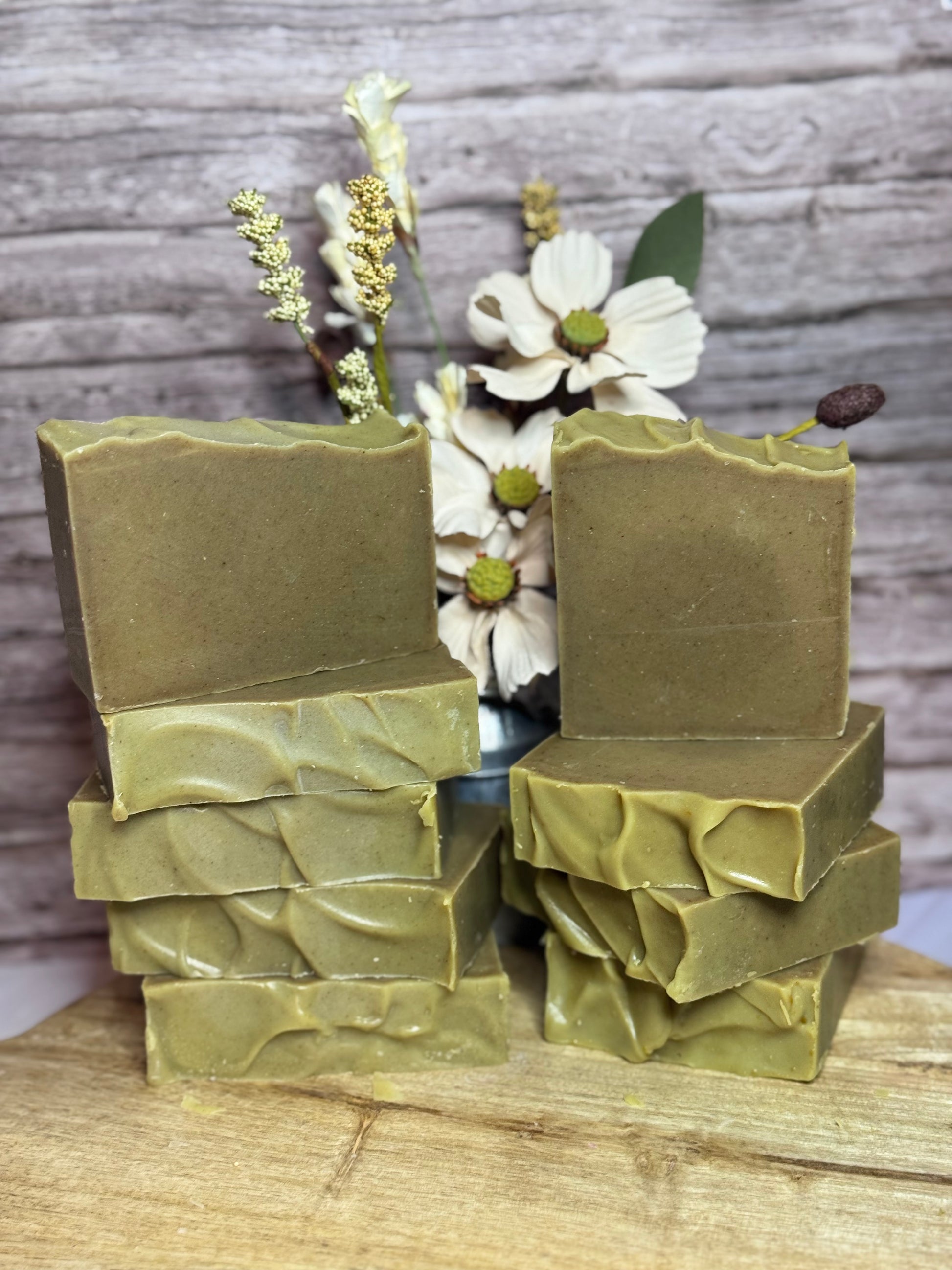 Stacks of green soap bars on a wooden surface with flowers in the background