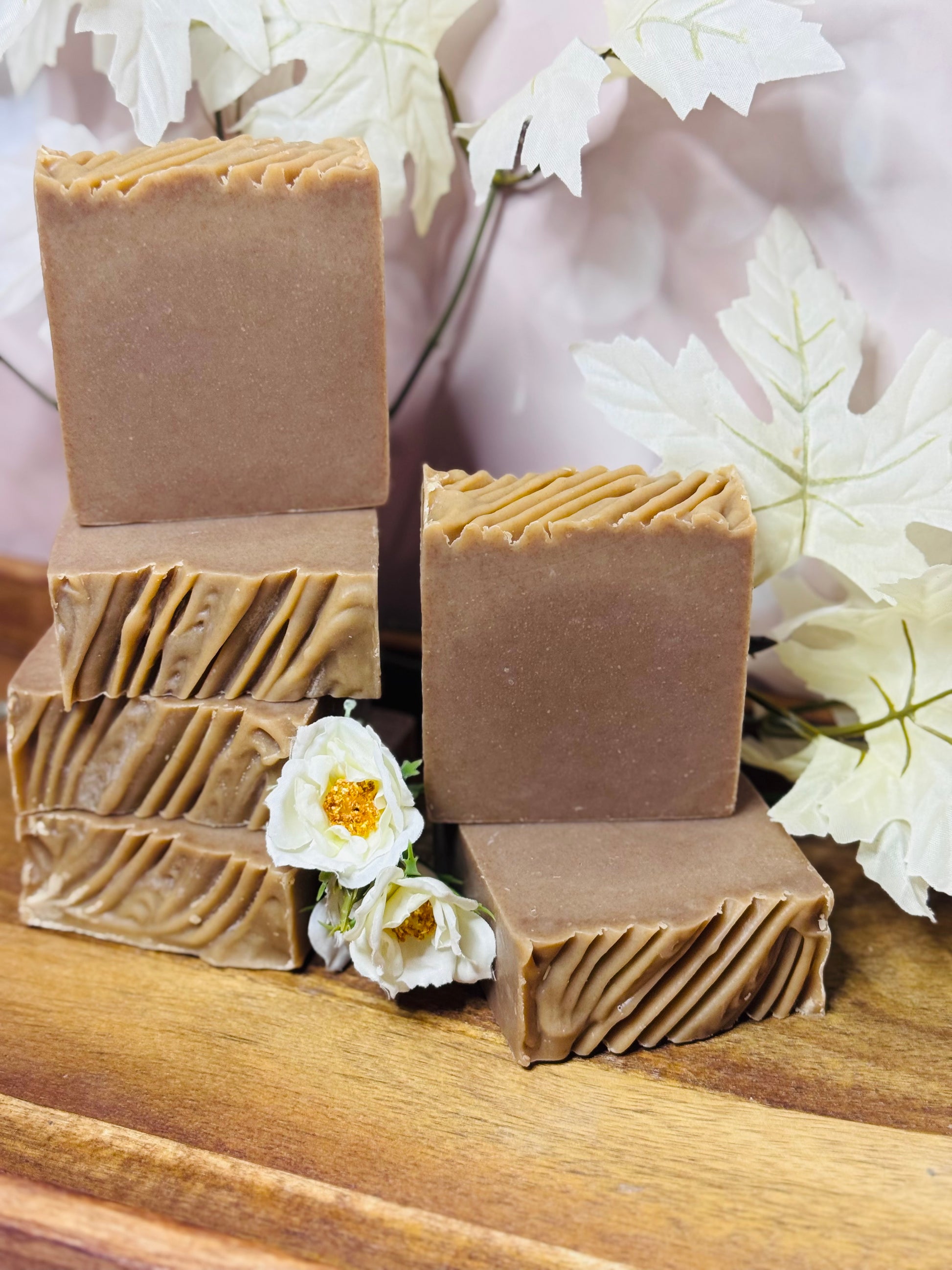 Stack of brown soap bars on a wooden surface with white flowers in the background