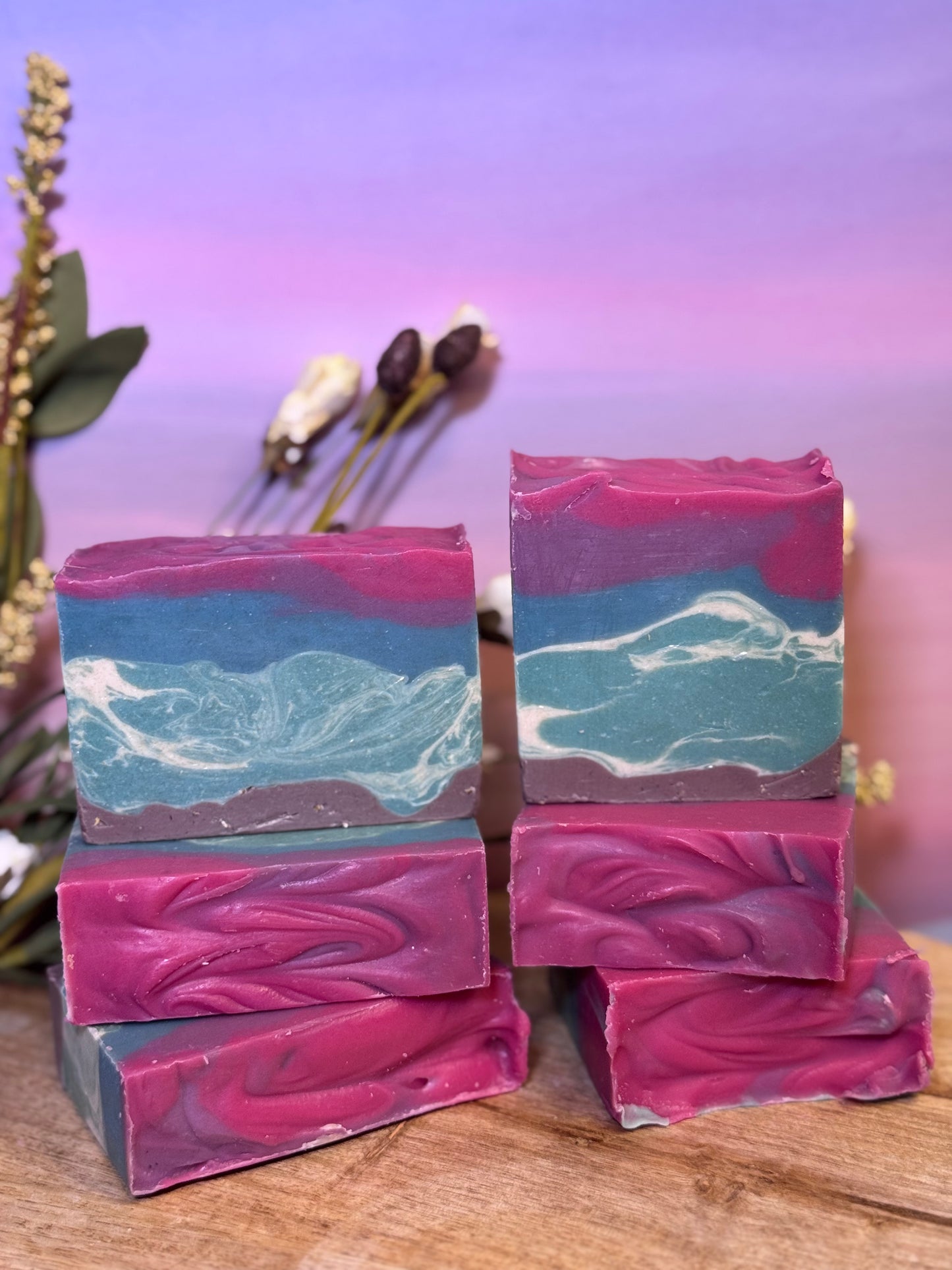 Stack of multicolored soap bars on a wooden surface with a blurred floral background