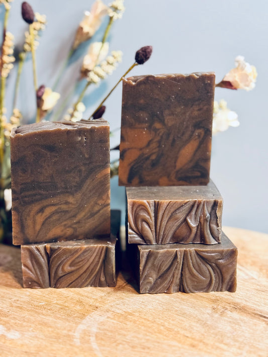 Stack of brown soap bars with decorative patterns on a wooden surface with a blurred floral background.