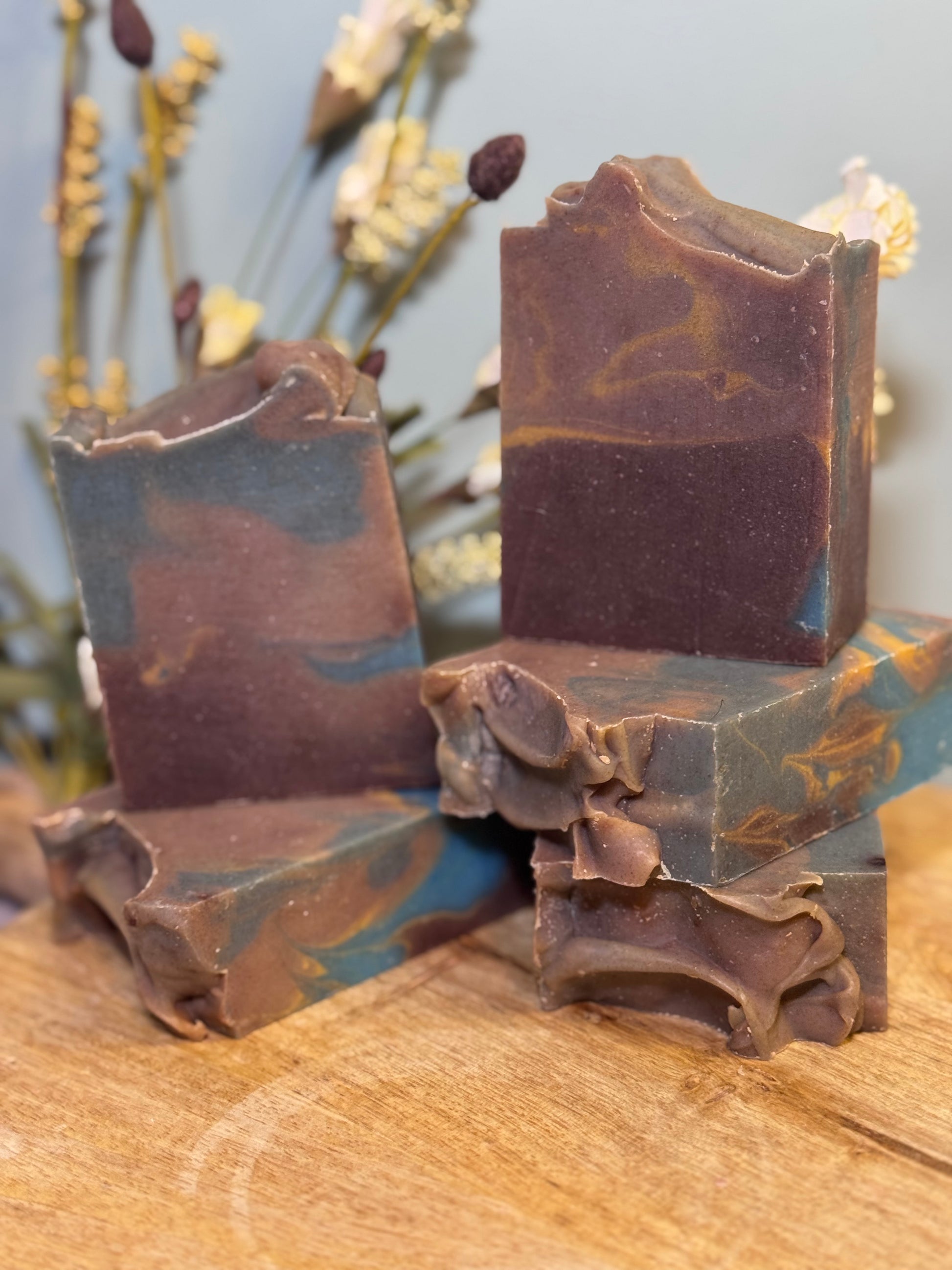 Five  bars of brown soap with decorative ruffles on a wooden surface.