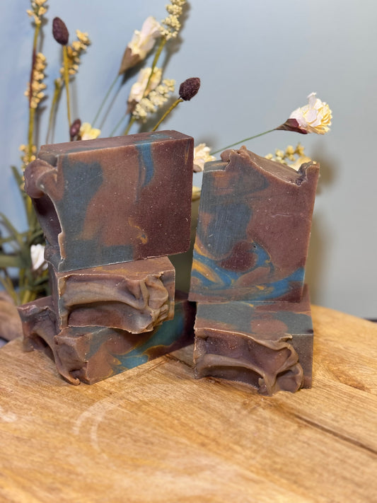 Five  bars of brown and blue soap on a wooden surface with a blurred plant background