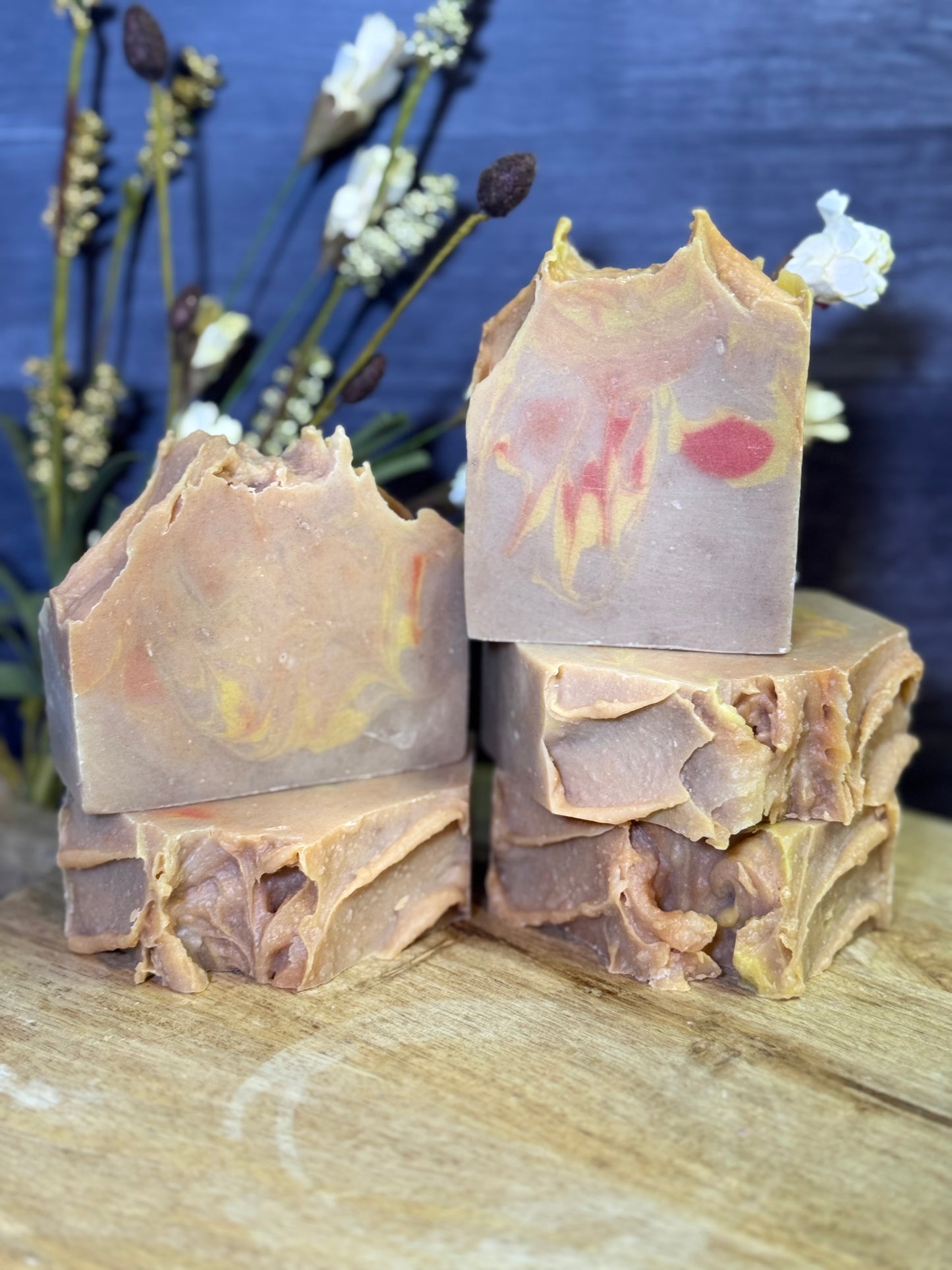 Five bars of soap with floral design on a wooden surface with a blue background and decorative plants.