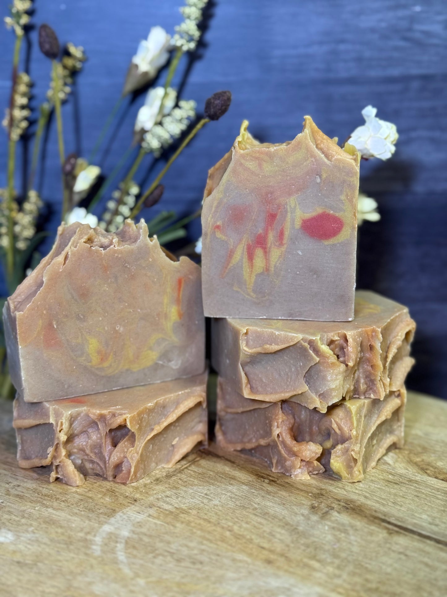 Five bars of soap with natural patterns on a wooden surface with a blurred floral background.