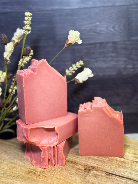 Four pink soap bars on a wooden surface with a dark background and small flowers.