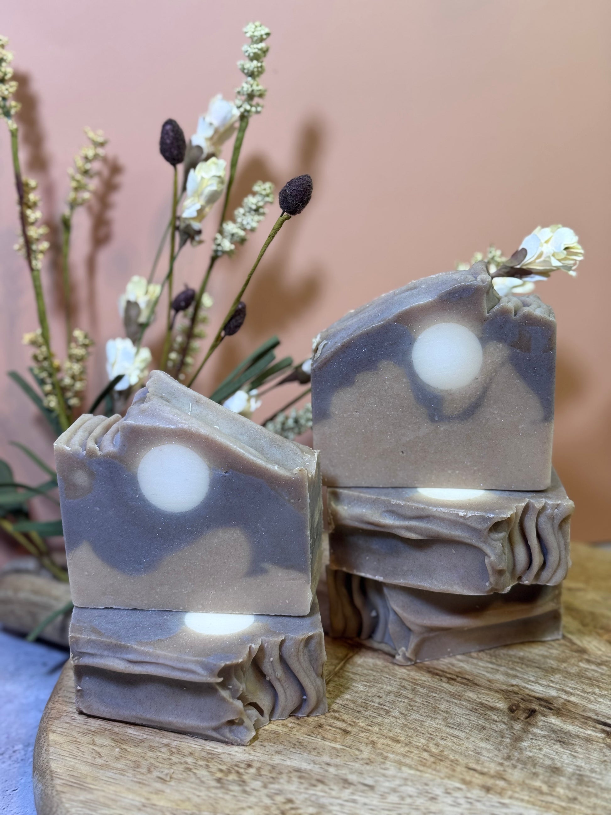 five bars of soap with a natural, earthy color on a wooden surface with a blurred background.