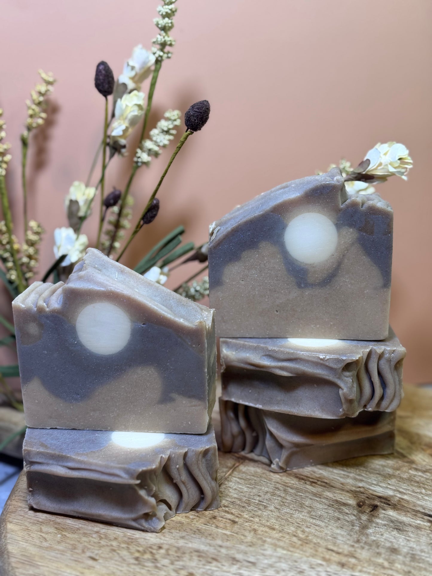 5  bars of soap with a natural pattern and a full moon on a wooden surface with flowers in the background.