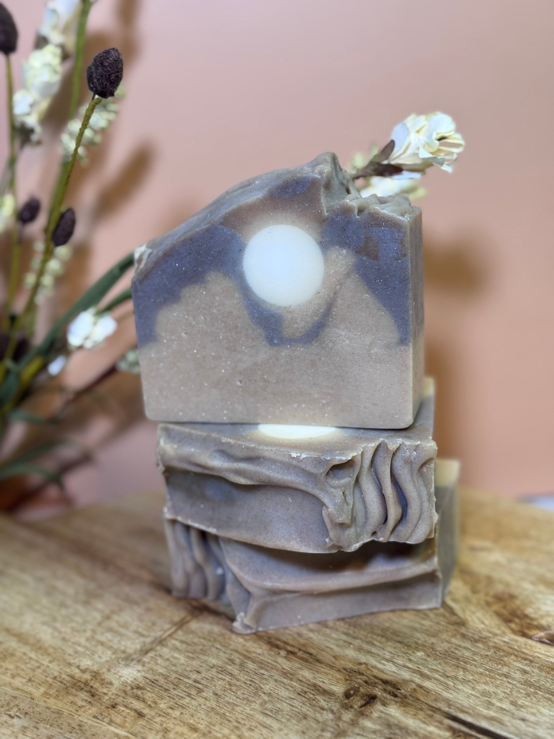 Stack of layered soap bars on a wooden surface with a blurred floral background