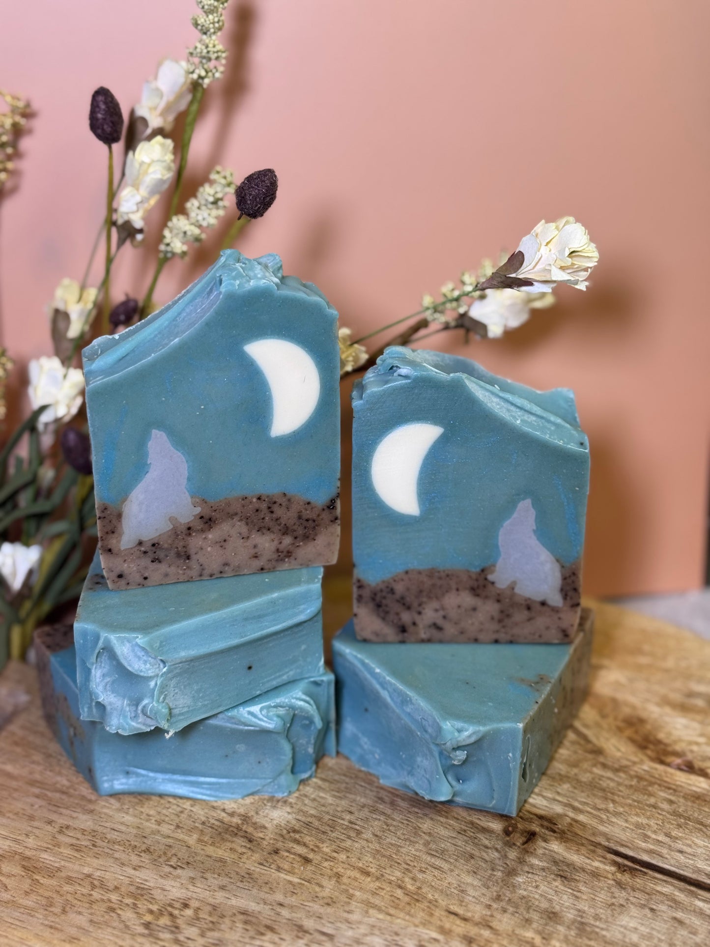 Five bars of soap with moon and wolf designs on a wooden surface.
