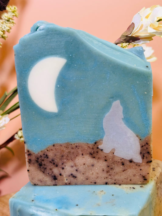 Soap bar with a wolf and moon design on a decorative stand with flowers in the background