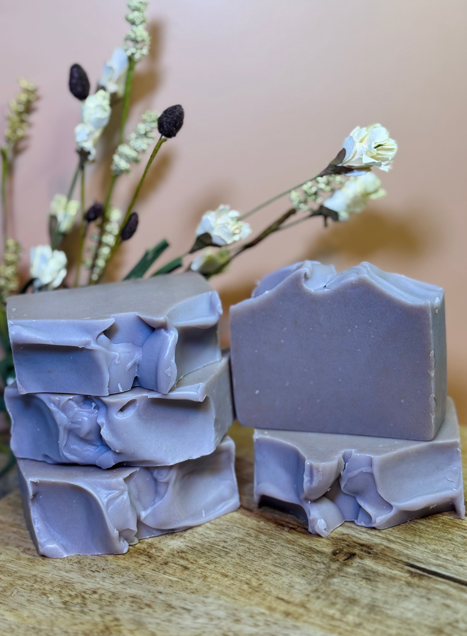 Stack of lavender-colored soap bars on a wooden surface with a blurred floral background