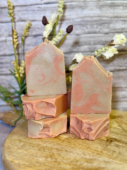 five bars of soap with a marbled pattern on a wooden surface with flowers in the background.