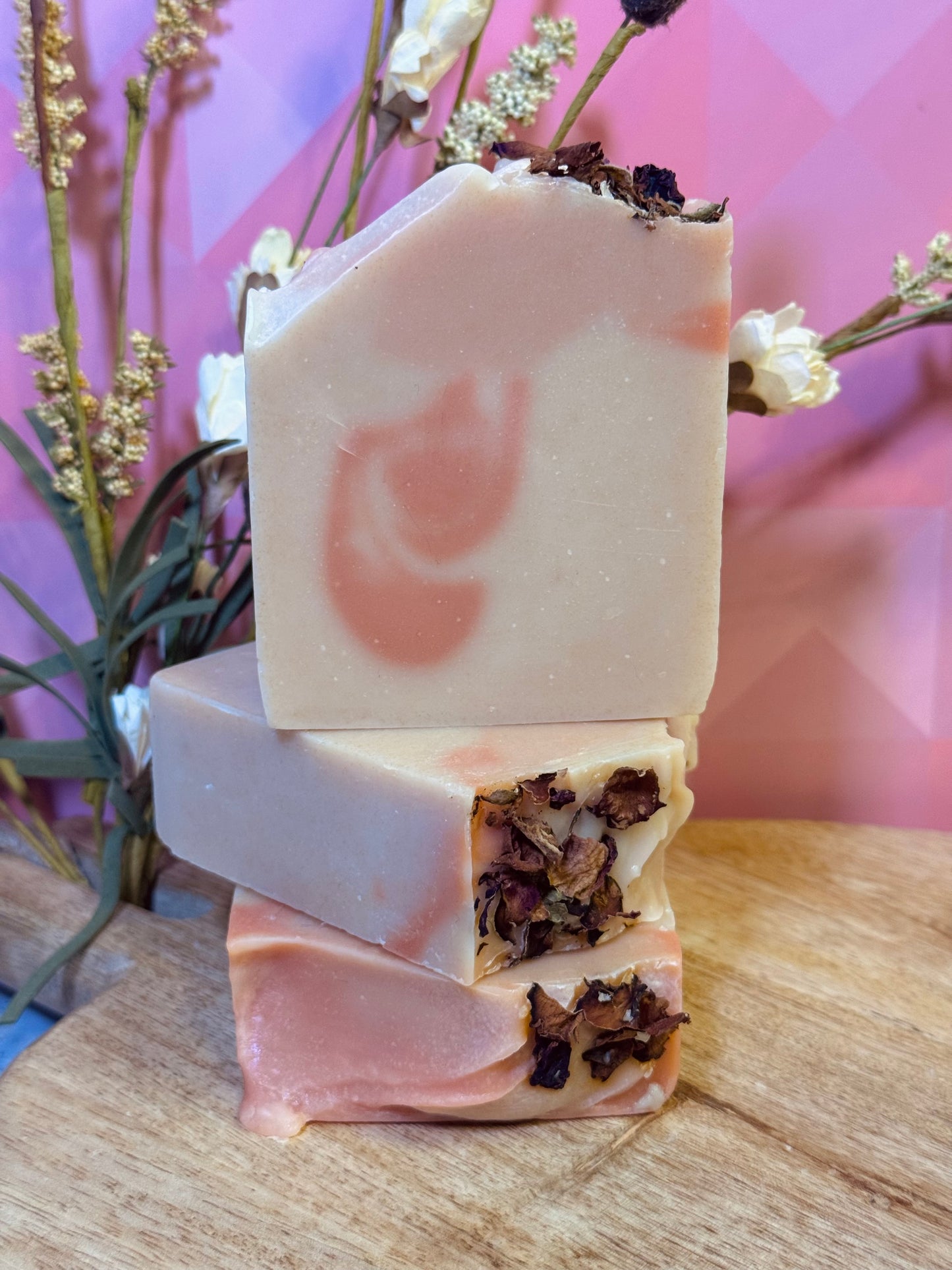 Stack of three handmade soap bars with natural ingredients on a wooden surface.