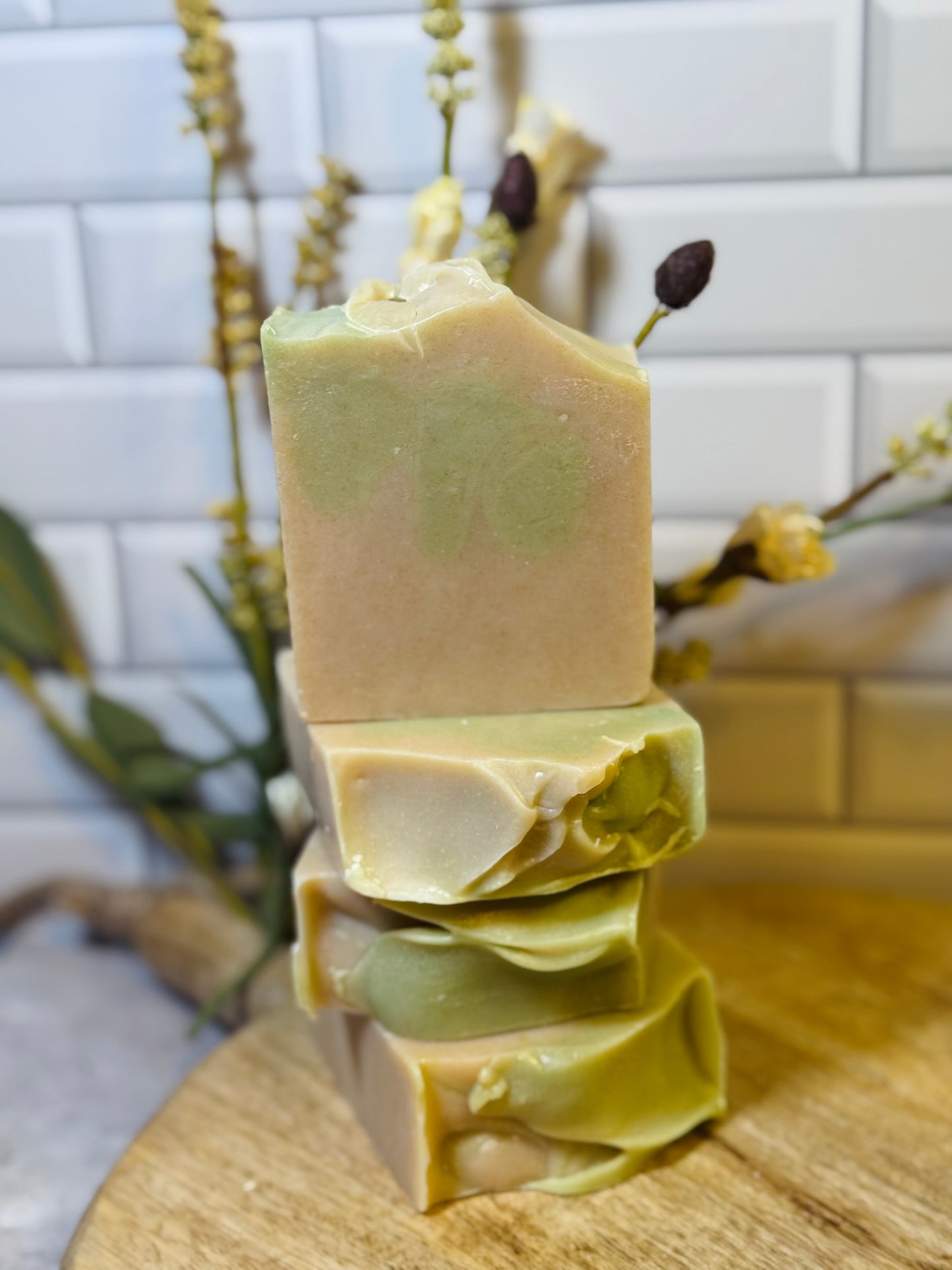 Stack of green soap bars on a wooden surface with a white tiled wall in the background