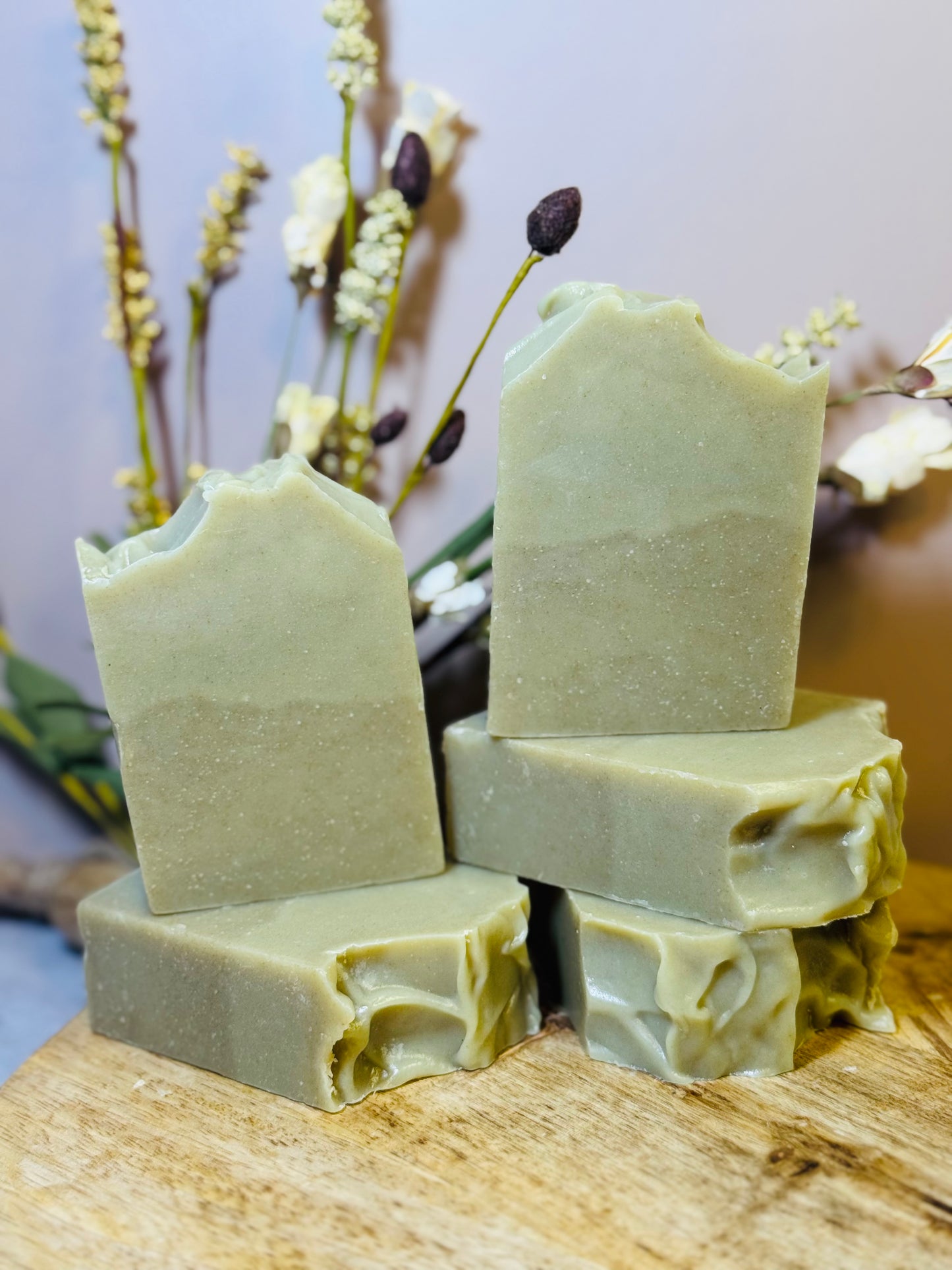 Stack of green soap bars on a wooden surface with a blurred natural background