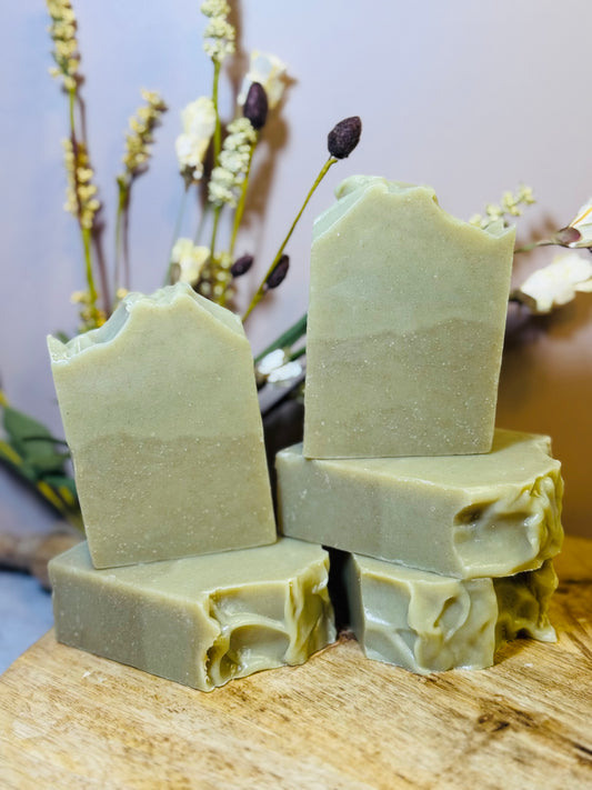 Stack of green soap bars on a wooden surface with a blurred natural background
