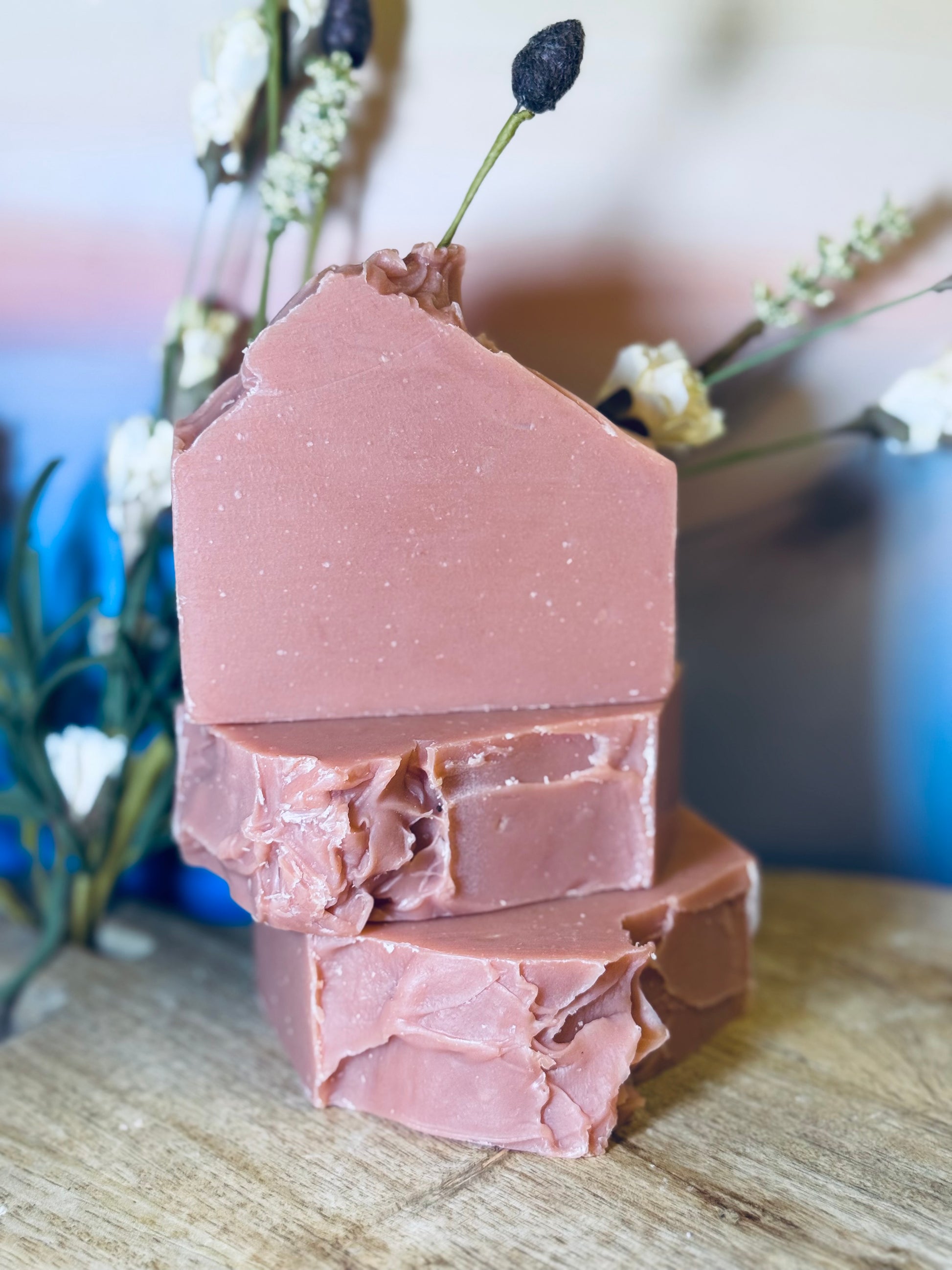 Stack of pink soap bars on a wooden surface with blurred flowers in the background