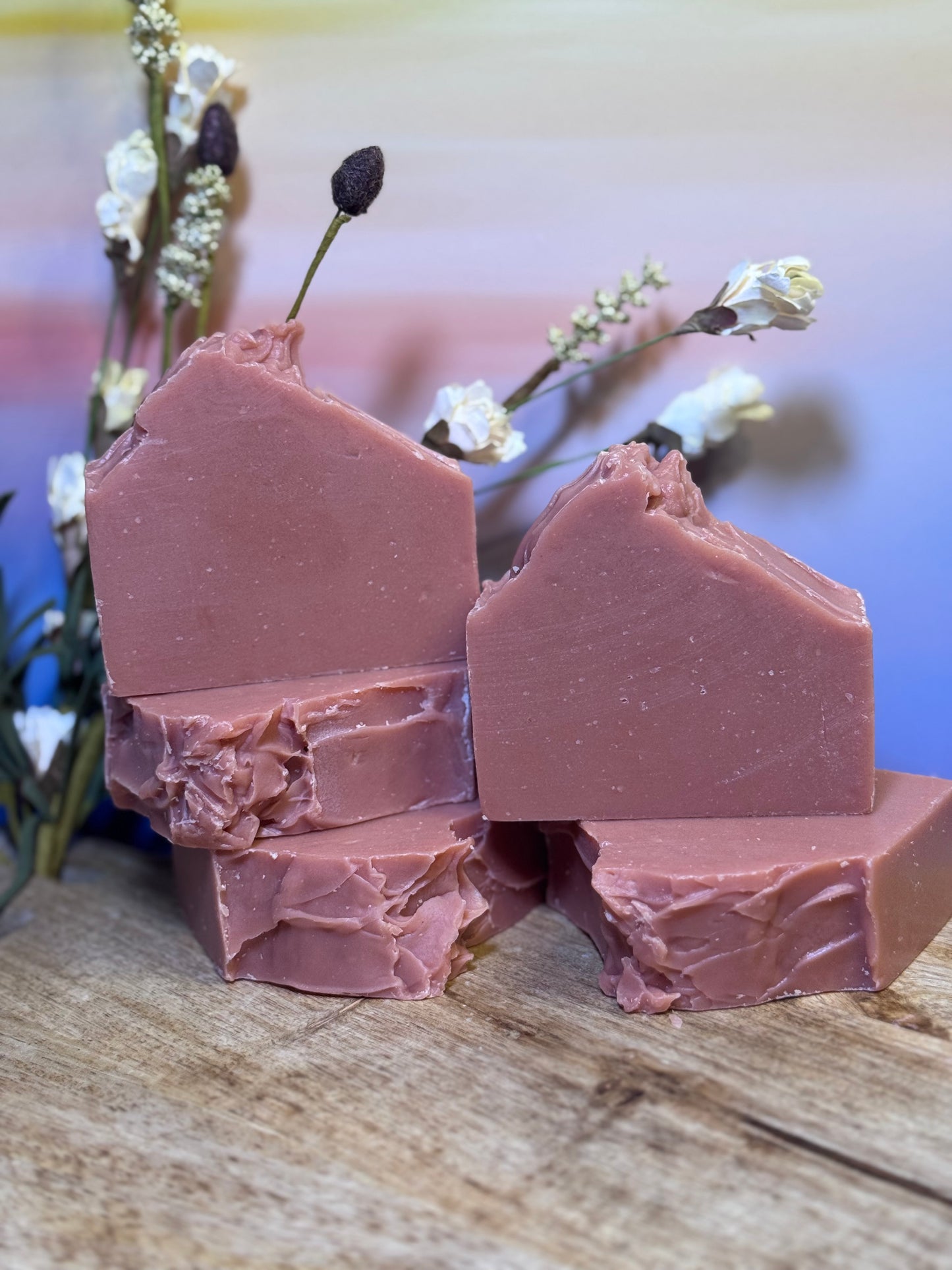 Pink soap bars on a wooden surface with flowers in the background
