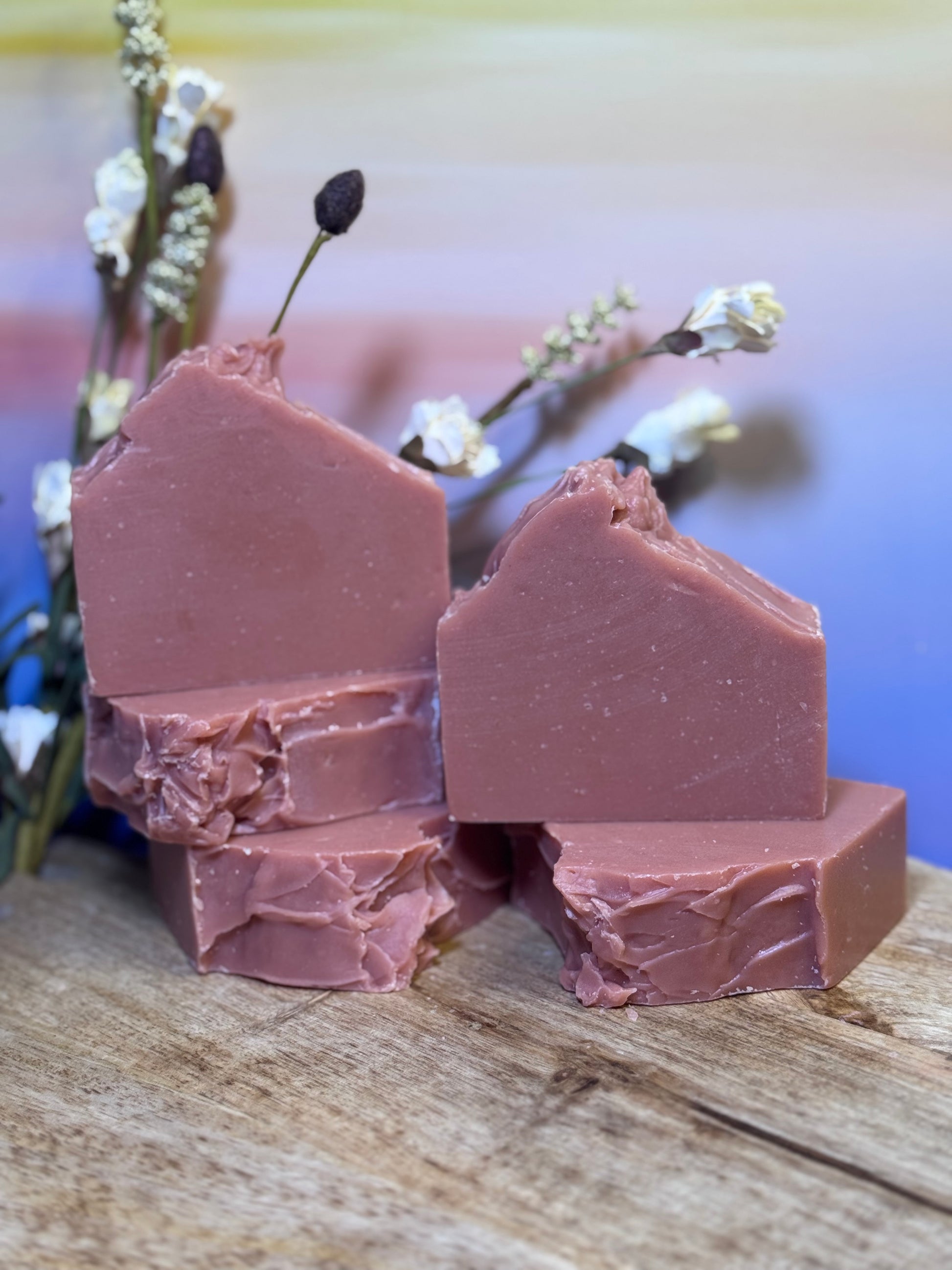 Five pieces of pink soap on a wooden surface with a blurred natural background