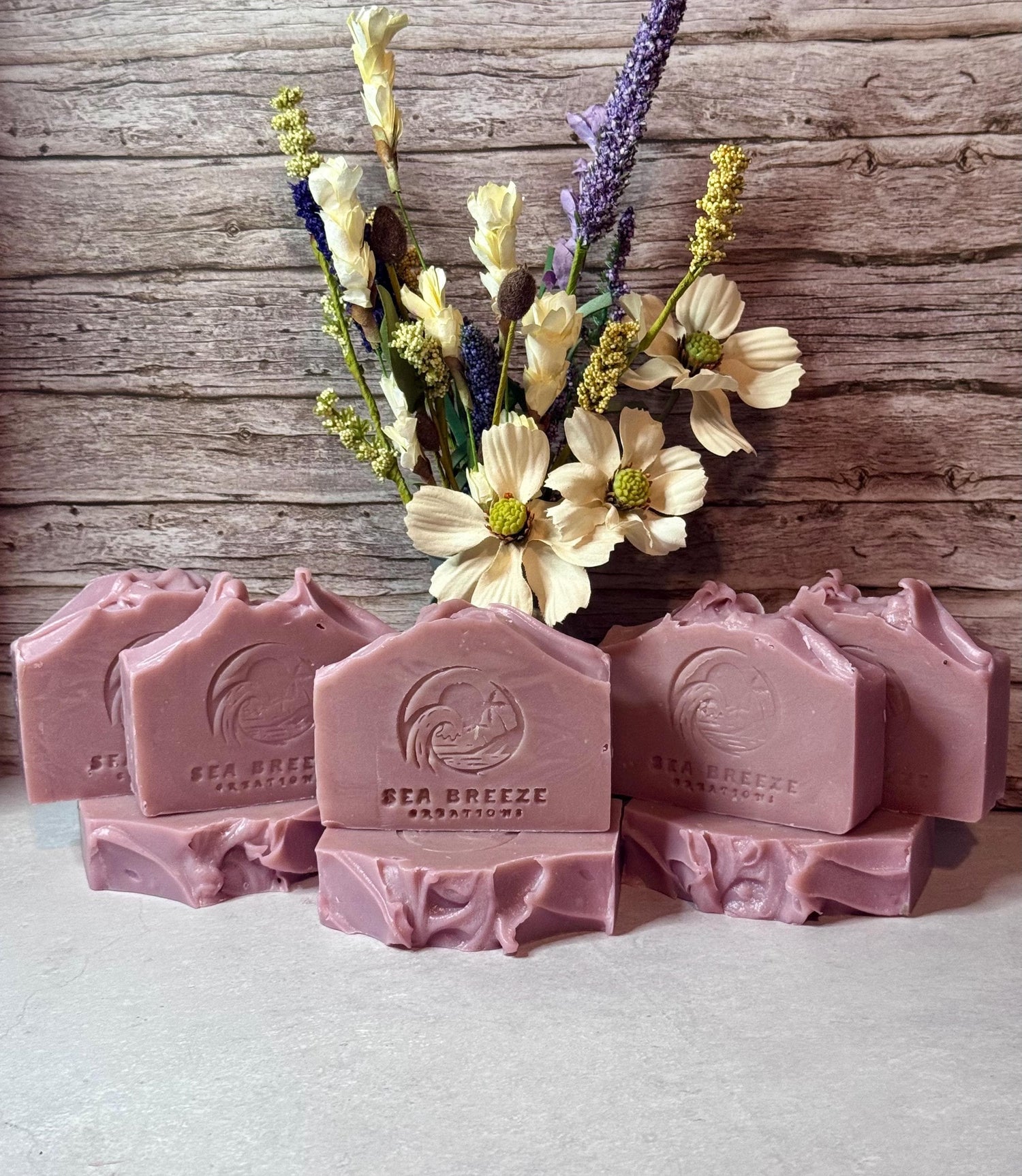 Pink soap bars with a logo on a white surface, accompanied by a bouquet of flowers against a wooden background.